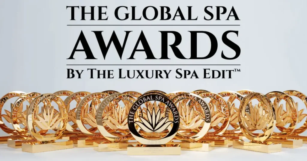 The words "THE GLOBAL SPA AWARDS BY THE LUXURY SPA EDIT™" in bold, black text positioned above a display of numerous shiny gold trophies. Each circular trophy features a central lotus flower motif and is engraved with the text "THE GLOBAL SPA AWARDS 2026"